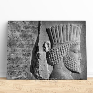 May include: A black and white photograph of a stone relief carving of a king's head wearing a crown. The carving is detailed and shows the king's face, beard, and crown. The background is a stone wall with cuneiform writing.