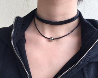 May include: A black leather choker necklace with a silver bead accent. The necklace is layered with a second, thinner black choker.