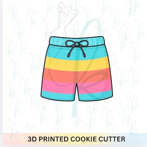 May include: A 3D printed cookie cutter in the shape of colorful swim trunks. The trunks are turquoise, with horizontal stripes of yellow, orange, and pink. The waistband has a black drawstring. The text "3D PRINTED COOKIE CUTTER" is at the bottom.