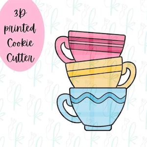 May include: A 3D printed cookie cutter shaped like a stack of three teacups. The top cup is pink with horizontal lines, the middle cup is yellow with a central band, and the bottom cup is light blue with a wavy line pattern. Text reads 3D printed Cookie Cutter.