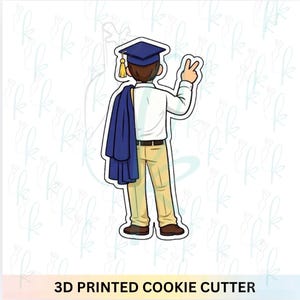 May include: A 3D printed cookie cutter in the shape of a person in a graduation cap and gown, with the text "3D PRINTED COOKIE CUTTER" at the bottom. The person is wearing a blue cap and gown, a white shirt, and khaki pants.