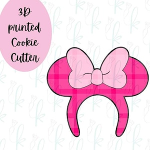 May include: A 3D printed cookie cutter shaped like a headband with two circular ears and a central bow. The design features a bright pink plaid pattern across the ears and a solid light pink colour on the bow. The text 3D printed Cookie Cutter is visible.