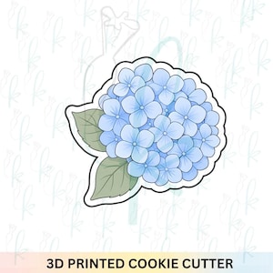 May include: A 3D printed cookie cutter shaped like a hydrangea flower. The design features a cluster of light blue, four-petaled blossoms with two sage green leaves at the base, all outlined in a thick black border against a white background.