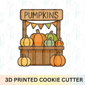May include: A 3D printed cookie cutter shaped like a wooden pumpkin stand with a sign that reads PUMPKINS. The design features a brown wooden stall, orange and green pumpkins of various sizes, and a decorative bunting banner in orange and green.