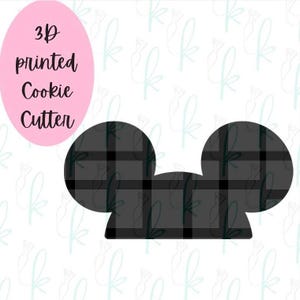 Puede incluir: Un cortador de galletas impreso en 3D en forma de orejas de Mickey Mouse, con estampado de cuadros negros y blancos. El texto "3D printed Cookie Cutter" está escrito en rosa sobre un fondo blanco.