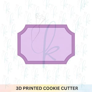 May include: A lavender-colored, rectangular cookie cutter with a decorative border. The text "3D PRINTED COOKIE CUTTER" is printed in black at the bottom of the image. The background features a repeating pattern of light blue floral designs.