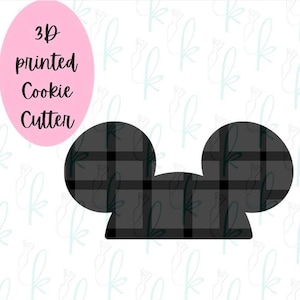 May include: A 3D printed cookie cutter shaped like a mouse head with two circular ears. The surface of the cutter features a black and dark gray plaid pattern. A pink oval in the upper left corner contains the text 3D printed Cookie Cutter.