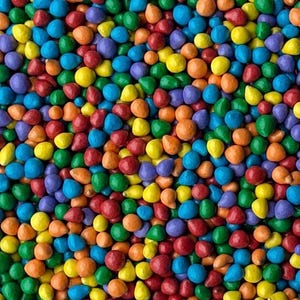 May include: A vibrant assortment of colorful, candy-coated chocolates. The image showcases a dense collection of small, pebble-shaped candies in a variety of hues, including red, orange, yellow, green, blue, and purple. The candies are evenly distributed, creating a visually appealing pattern.