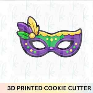 May include: A 3D printed cookie cutter in the shape of a Mardi Gras mask. The mask is purple with green and yellow accents, and features a feather detail. The text "3D PRINTED COOKIE CUTTER" is at the bottom.