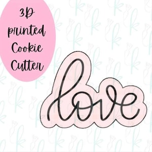 May include: A light pink 3D printed cookie cutter shaped like the word love in a cursive script font. The text 3D printed Cookie Cutter is displayed in black on a light pink oval background to the upper left of the cookie cutter shape.