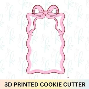 Puede incluir: Cortador de galletas rosa impreso en 3D con forma de marco rectangular con un lazo en la parte superior y lados ondulados en forma de cinta. El texto "3D PRINTED COOKIE CUTTER" está en la parte inferior.