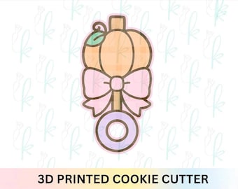 Puede incluir: Un cortador de galletas impreso en 3D con forma de calabaza con un lazo rosa y un asa circular. La calabaza es naranja con un patrón de cuadros y el lazo es de color rosa claro. El texto "3D PRINTED COOKIE CUTTER" está en la parte inferior.