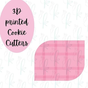 May include: A pink oval shape containing the black text 3D printed Cookie Cutters, positioned next to a pink and light pink plaid shape with rounded corners. The background features a repeating light blue line drawing of a piping bag.