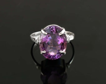 May include: A silver ring with a large, oval-shaped amethyst gemstone. The gemstone is a deep purple color and has a faceted cut. The ring is set in a simple, wire-wrapped style.
