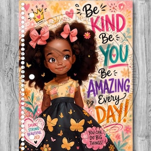 May include: A spiral-bound notebook cover featuring an illustration of a young girl with dark curly hair and pink bows, wearing a floral top and black butterfly-print dress. Text reads: Be KIND Be YOU Be AMAZING Every DAY! with additional motivational phrases.