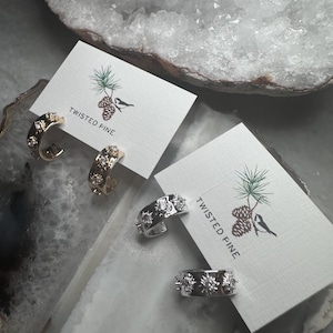 May include: Two pairs of hoop earrings with a starburst design. One pair is gold with clear rhinestones and the other pair is silver with clear rhinestones. The earrings are displayed on white cards with the logo "Twisted Pine".