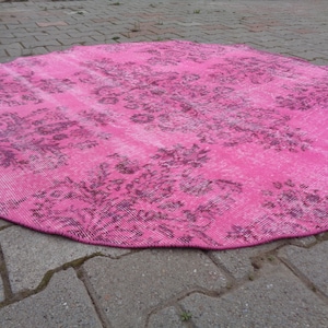 May include: A pink round rug with a floral pattern. The rug has a distressed look and is made of a soft, woven material.