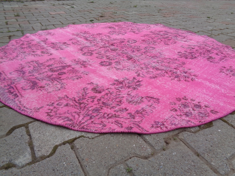 May include: A pink round rug with a floral pattern. The rug has a distressed look and is made of a soft, woven material.