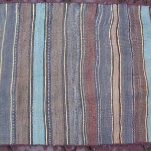May include: A striped rug with a variety of colors, including brown, blue, and yellow. The rug has a fringed edge.