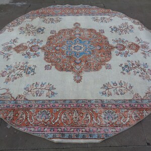 May include: A round, cream-colored rug with a floral pattern in shades of pink, blue, and orange. The rug has a border with a repeating pattern of stylized flowers and leaves.