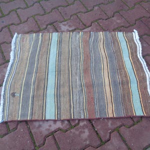 May include: A striped rug with brown, beige, blue, and white stripes. The rug has a white fringe border.