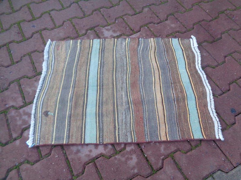 May include: A striped rug with brown, beige, blue, and white stripes. The rug has a white fringe border.