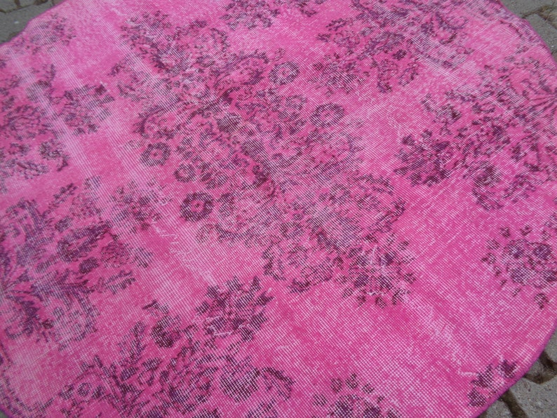May include: A round pink rug with a faded floral pattern in a darker shade of pink.