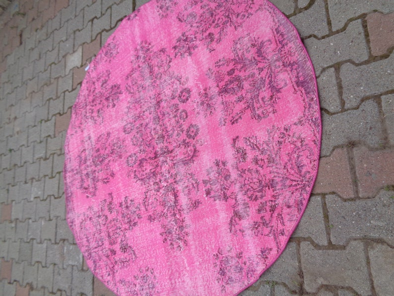 May include: A pink round rug with a floral pattern. The rug has a faded look, giving it a vintage feel.