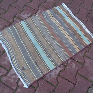 May include: A striped rug with a fringed edge. The rug has a variety of colors, including brown, beige, blue, and gray.