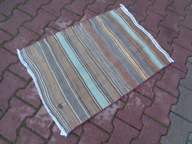 May include: A striped rug with a fringed edge. The rug has a variety of colors, including brown, beige, blue, and gray.
