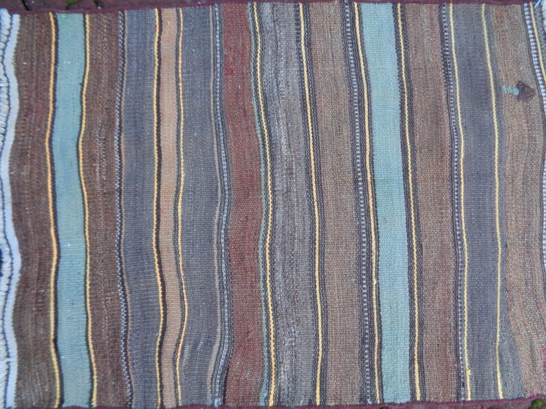 May include: A striped woven rug with a variety of colors, including brown, blue, and yellow. The rug has a fringed edge.
