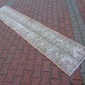 May include: A long, narrow rug with a beige background and a floral pattern in shades of brown, blue, and white. The rug is laid out on a brick patio.