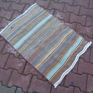 May include: A striped rug with a white fringe. The rug has shades of brown, blue, and beige.