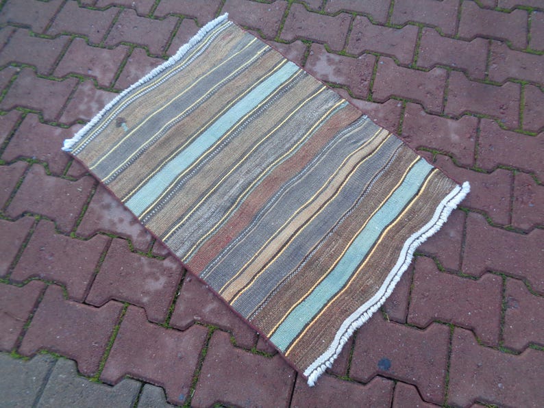 May include: A striped rug with a white fringe. The rug has shades of brown, blue, and beige.