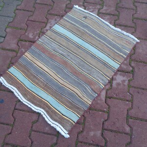 May include: A striped rug with a white fringe. The rug has shades of brown, blue, and beige.