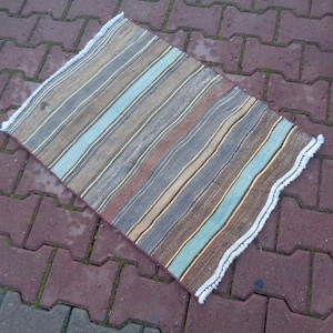 May include: A striped rug with a white fringe border. The rug has shades of brown, blue, and beige.