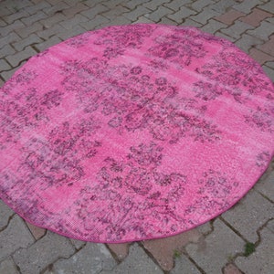 May include: A round pink rug with a floral pattern in a darker shade of pink. The rug has a distressed look, with some areas appearing faded.