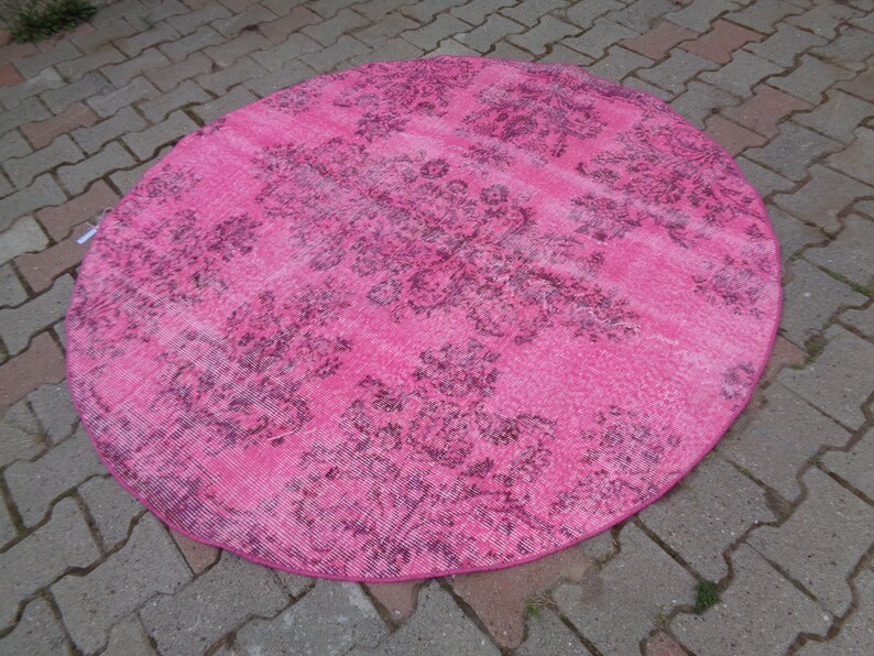 May include: A round pink rug with a floral pattern in a darker shade of pink. The rug has a distressed look, with some areas appearing faded.