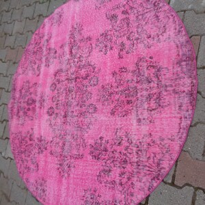 May include: A pink round rug with a dark floral pattern. The rug is made of a soft, textured material.