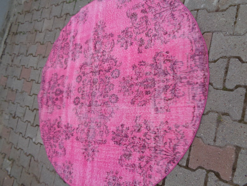 May include: A pink round rug with a dark floral pattern. The rug is made of a soft, textured material.