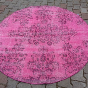 May include: A round pink rug with a faded floral pattern in a darker shade of pink. The rug has a distressed look and is perfect for adding a touch of vintage charm to any room.