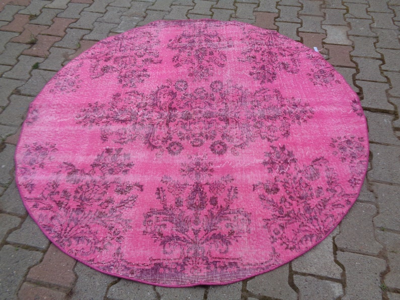 May include: A round pink rug with a faded floral pattern in a darker shade of pink. The rug has a distressed look and is perfect for adding a touch of vintage charm to any room.