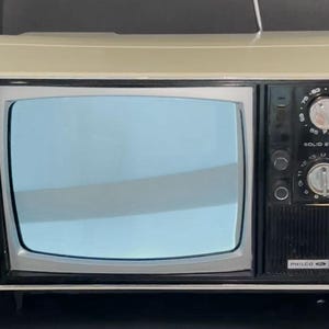 May include: A vintage Philco solid state television with a cream-colored plastic casing and a black control panel on the right side. The unit features two circular silver knobs for tuning, a small antenna, and a screen displaying a light blue tint.