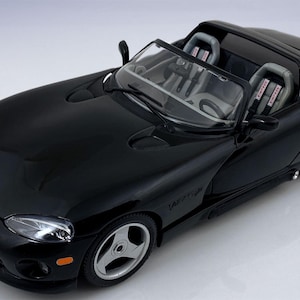Puede incluir: Modelo de un descapotable Dodge Viper negro brillante. El coche tiene ruedas plateadas, un interior detallado con asientos de carreras y el logotipo Viper en la parte delantera. El modelo es una elegante representación de un coche deportivo.