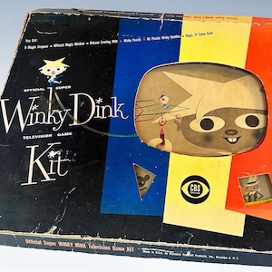 May include: A vintage Winky Dink television game kit box featuring a black, blue, yellow, and orange color scheme. The box displays the text Official Super Winky Dink Television Game Kit, a cartoon character illustration, and a CBS Television logo.