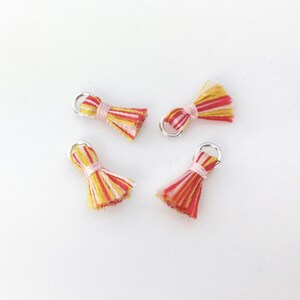 May include: Four small, colorful tassels with silver jump rings. The tassels are made of pink, yellow, and red yarn.