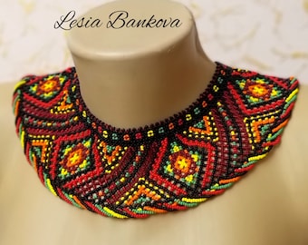 May include: A colourful beaded choker necklace with a geometric pattern in shades of red, yellow, green, and black. The necklace is on a mannequin.