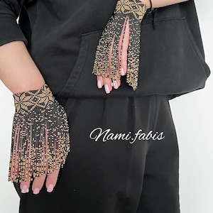 May include: Black and gold beaded wrist cuffs with fringe detail. The cuffs feature a geometric pattern and are worn on the wrists. The image also includes the text "Nami.fabis".