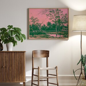 Puede incluir: Una pintura de paisaje enmarcada con un cielo rosa y &aacute;rboles verdes reflejados en un cuerpo de agua tranquilo. La pintura est&aacute; colgada en una pared blanca sobre un gabinete de madera.
