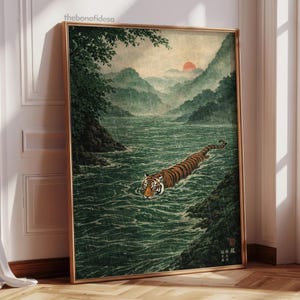 May include: A framed art print showing a tiger swimming in a river, with mountains and a setting sun in the background. The artwork is in a traditional Japanese style, with muted greens, browns, and oranges. The frame is gold.